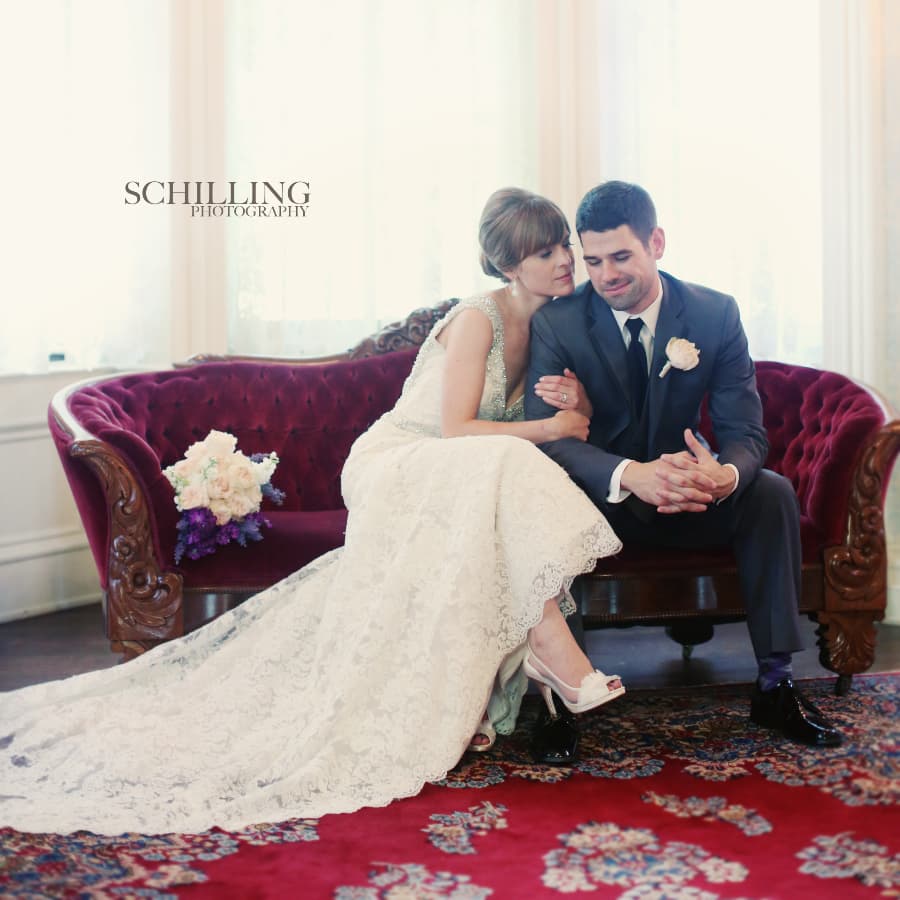 A bride and groom tenderly embrace on a vintage sofa, surrounded by soft natural light.
