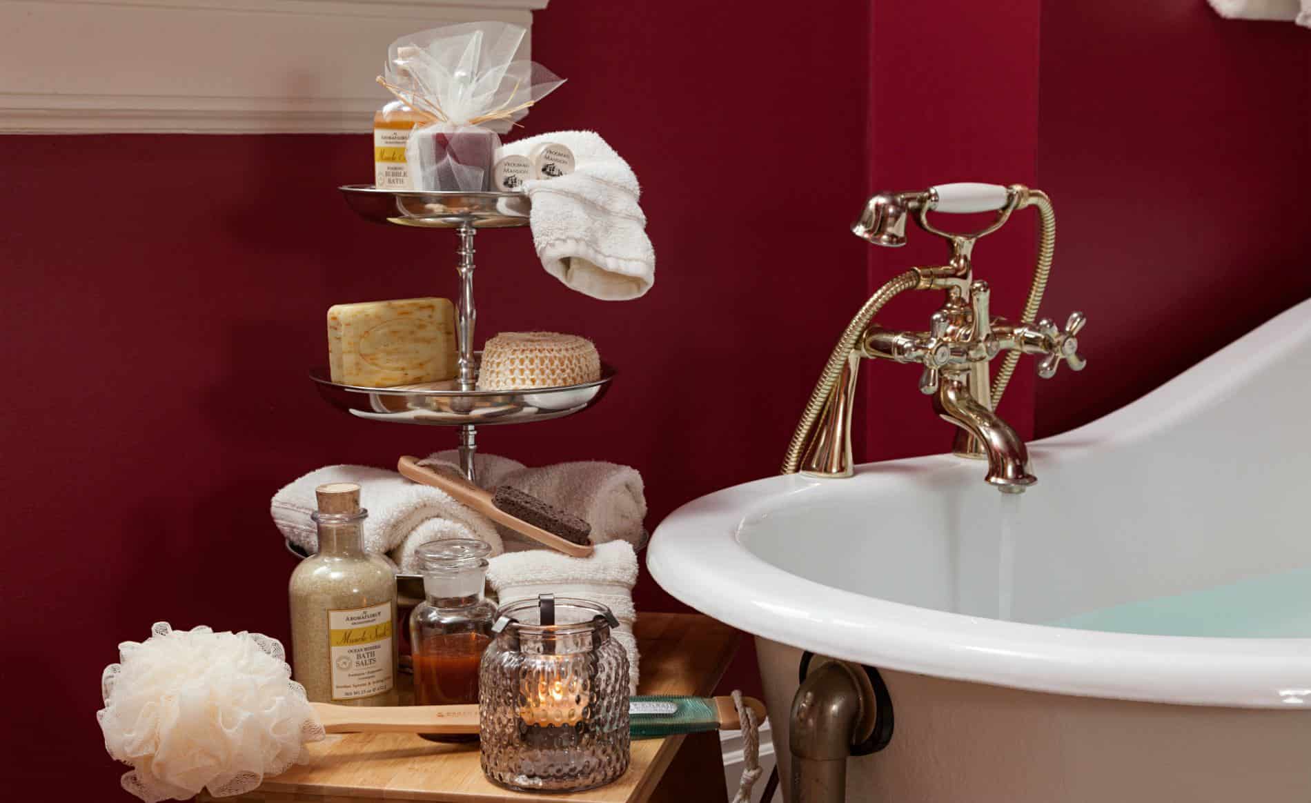 Close-up view of white clawfoot tub in red room and a wood stool topped with white towels and various toiletries