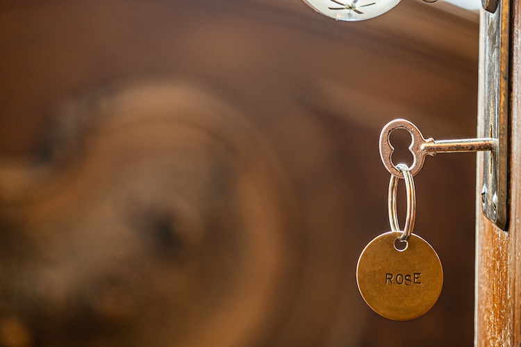 Close of up engraved vintage key in the lock with the chain that says Rose and the ornamental footboard in the background