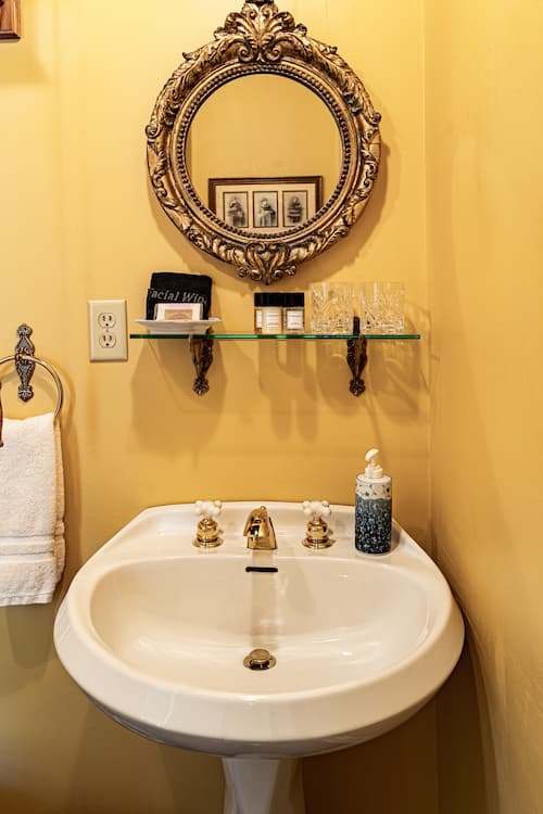 Pedestal sink, gold outlined mirror and shelf with overnight amentities