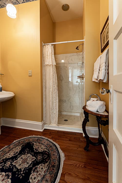 Private bathroom with warm yellow walls, walk in shower and plush white towels
