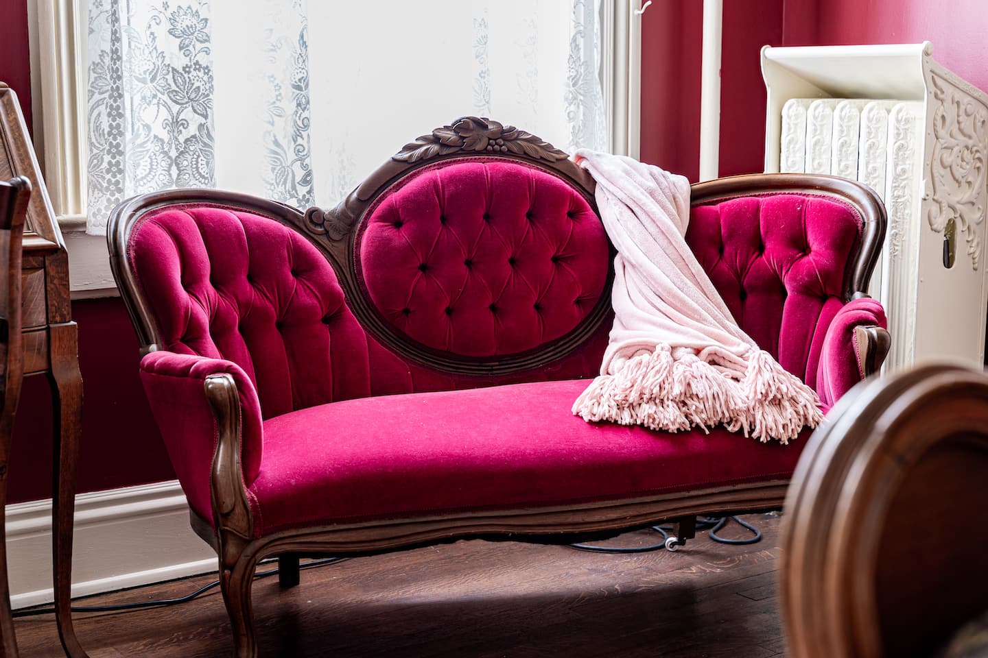 A small, antique-style settee upholstered in vibrant magenta velvet and featuring a carved dark wood frame with ornate detailing along the back and arms.
