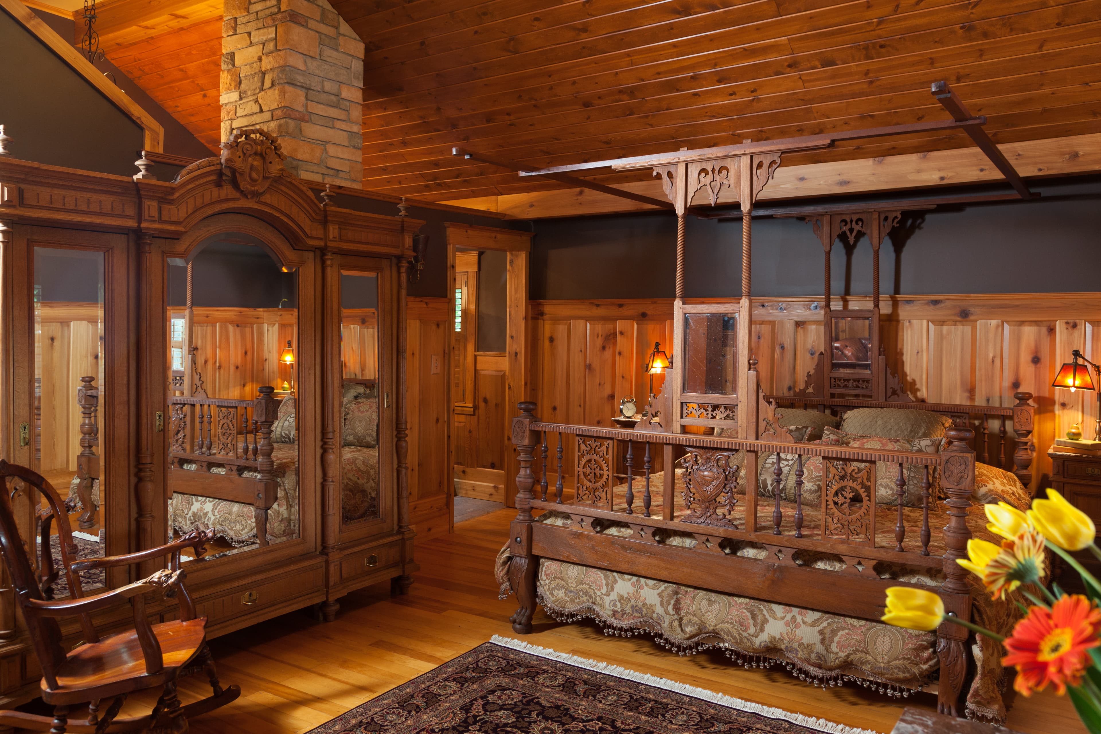 A rustic-style bedroom with ornate wooden king size bed and large mirrored armoire.