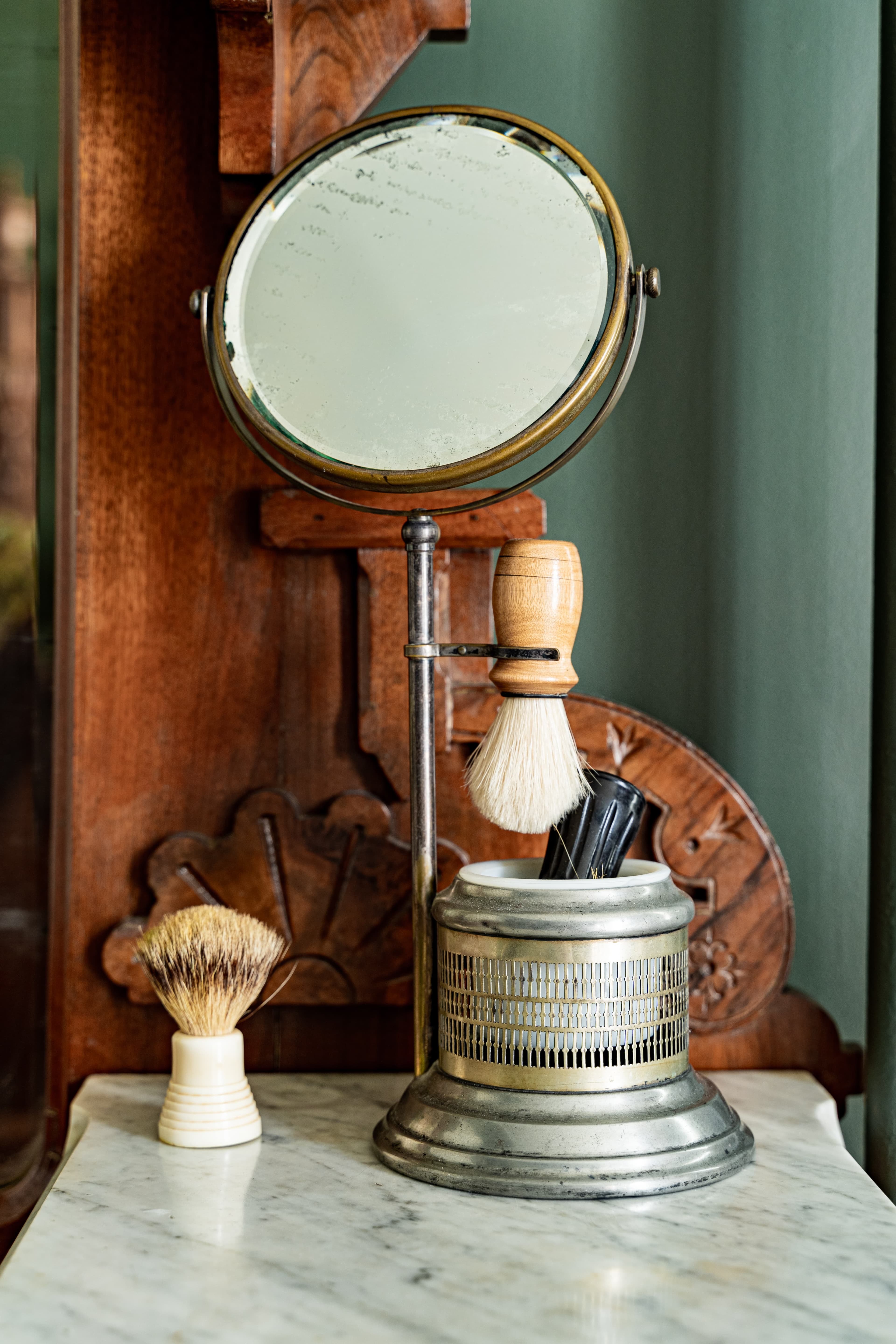 Antique shaving set with silver mug, wooden handled brushes, and tilting mirror tops the dresser