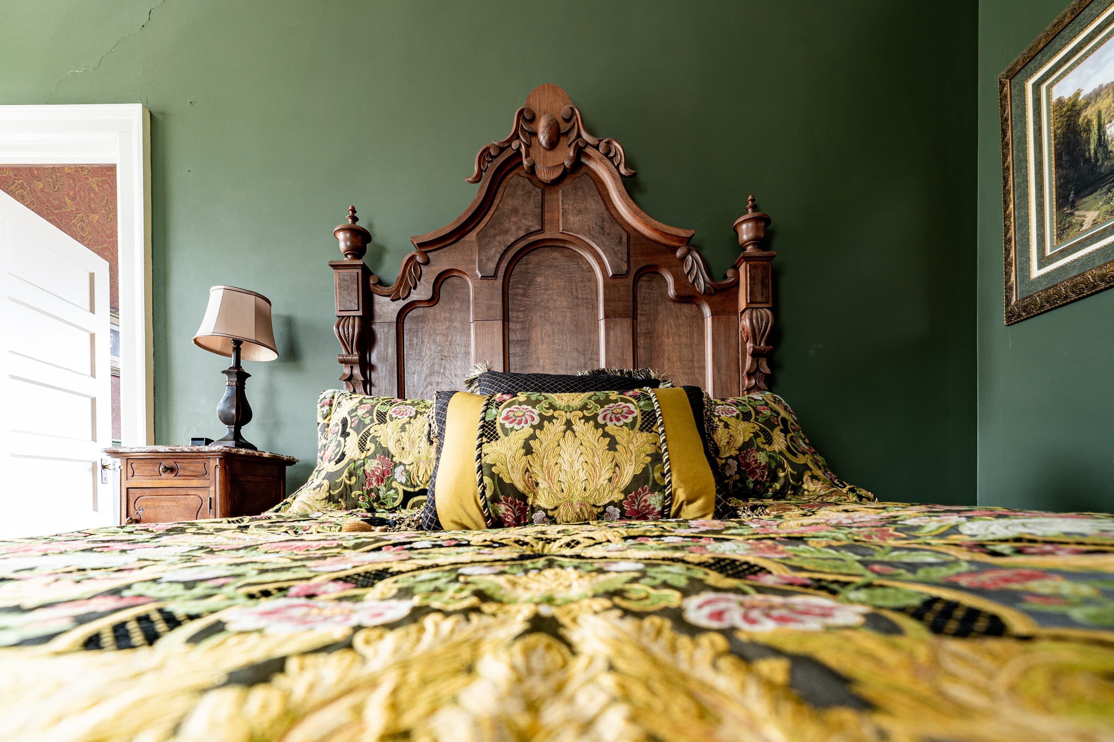 Detail of queen size bed with yellow floral bedding and antique wooden headboard