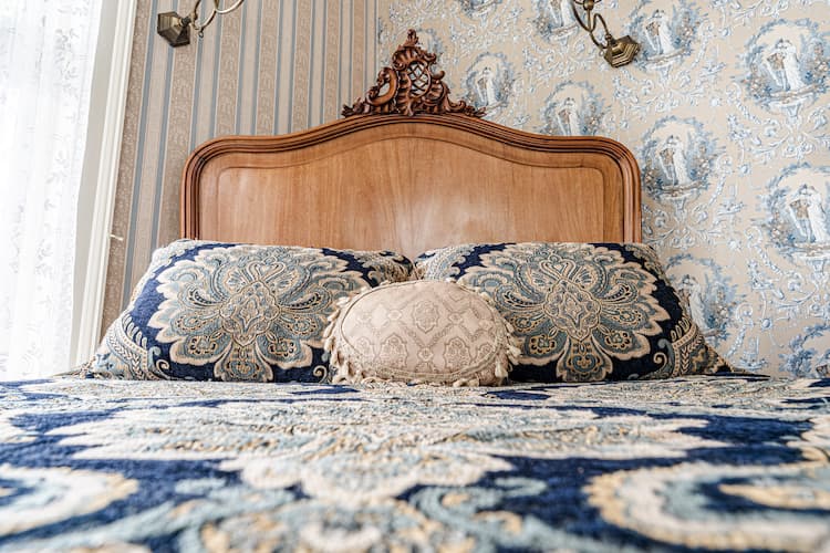 Close up of Julia's queen size bed with blue and cream vintage style pillows and bedspread; west facing window in background