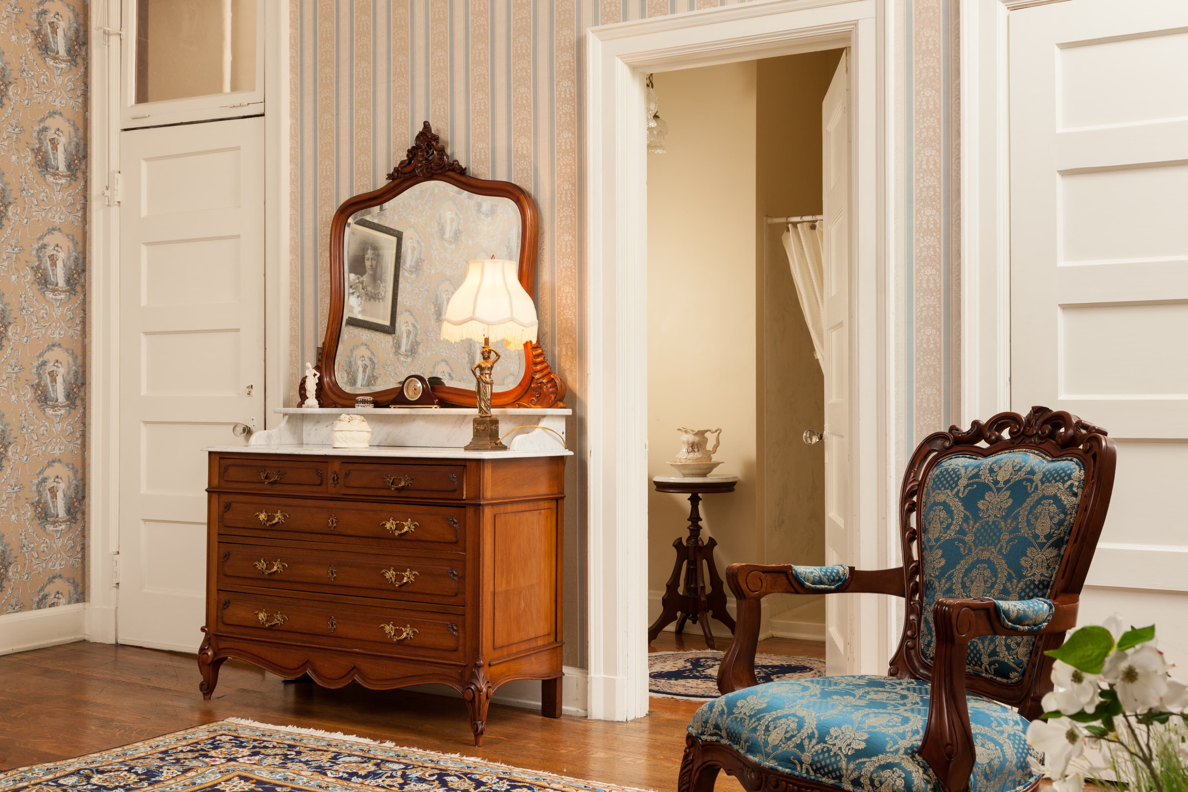 Antique wooden dresser and comfortable antique armchair in Julia's Suite near bathroom door; view of bathroom and walk in shower.