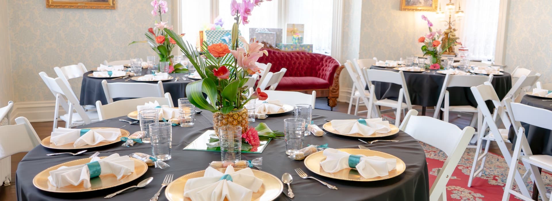 A beautifully decorated dining area with round tables set for an event, featuring floral centerpieces and elegant tableware.