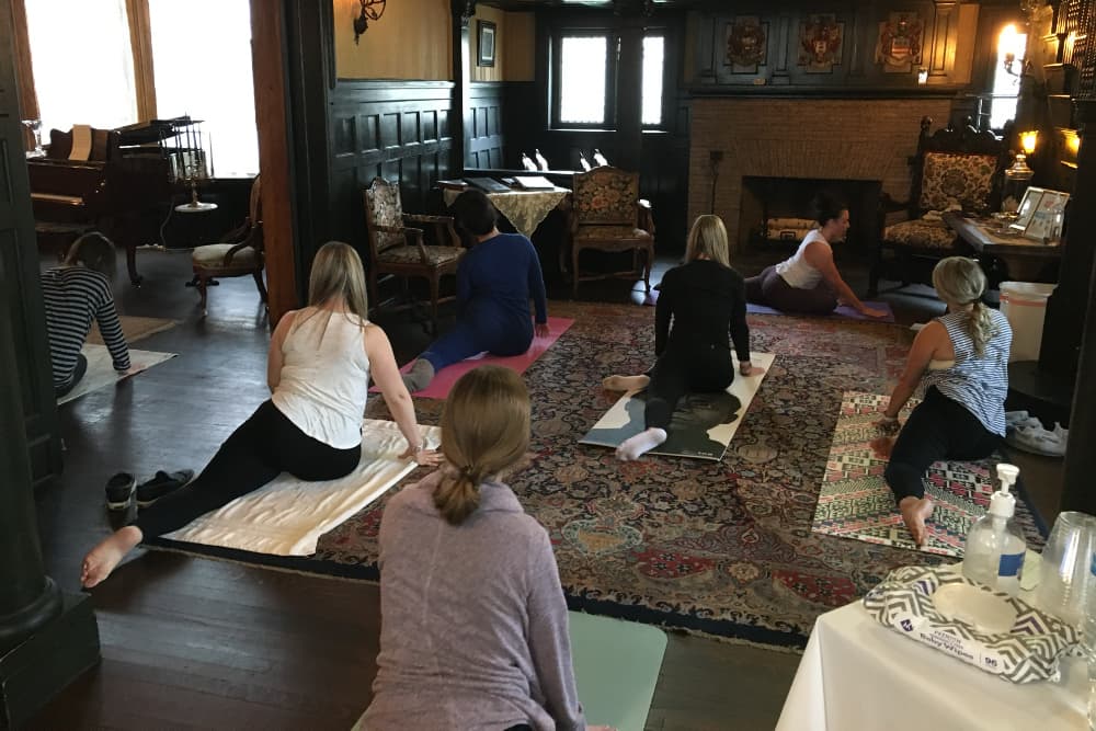 A group of people practicing yoga in a cozy room with a piano and ornate furnishings.