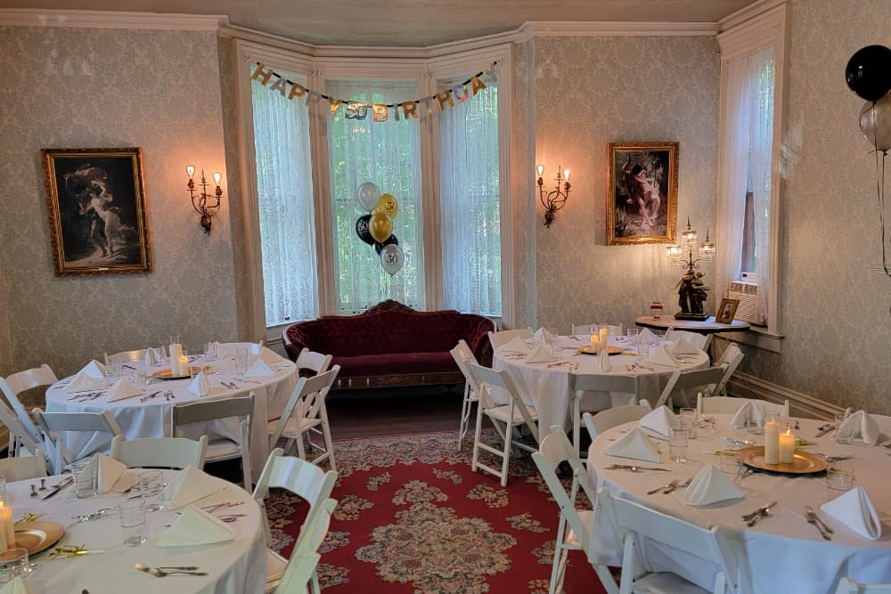 A decorated birthday celebration room featuring round tables, a vintage sofa, and festive balloons.