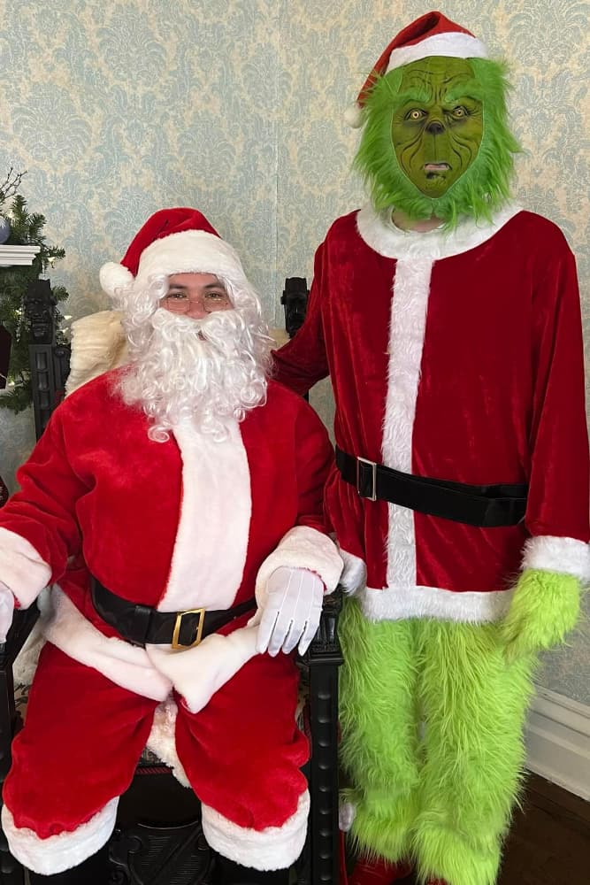 A man in a Santa costume sits next to a person dressed as the Grinch.