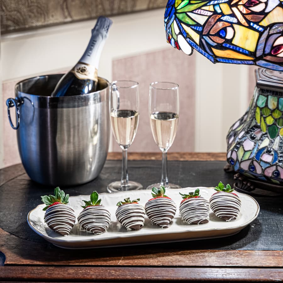 A platter of chocolate-covered strawberries is arranged alongside two flutes of champagne and a silver ice bucket.
