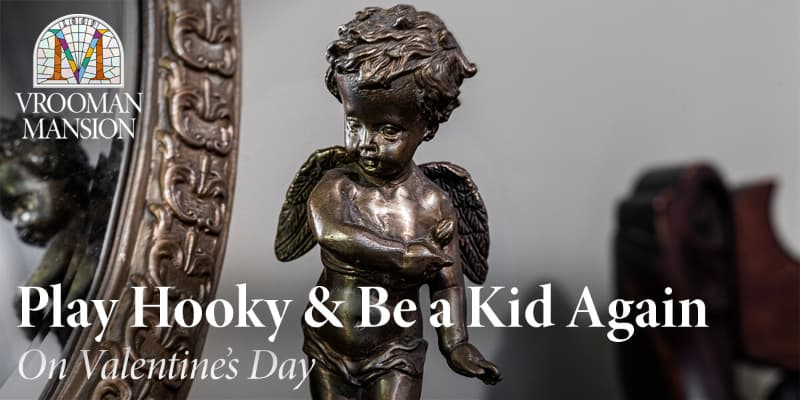 A close-up of a bronze cherub statue next to an ornate mirror, promoting a Valentine's Day event at Vrooman Mansion.