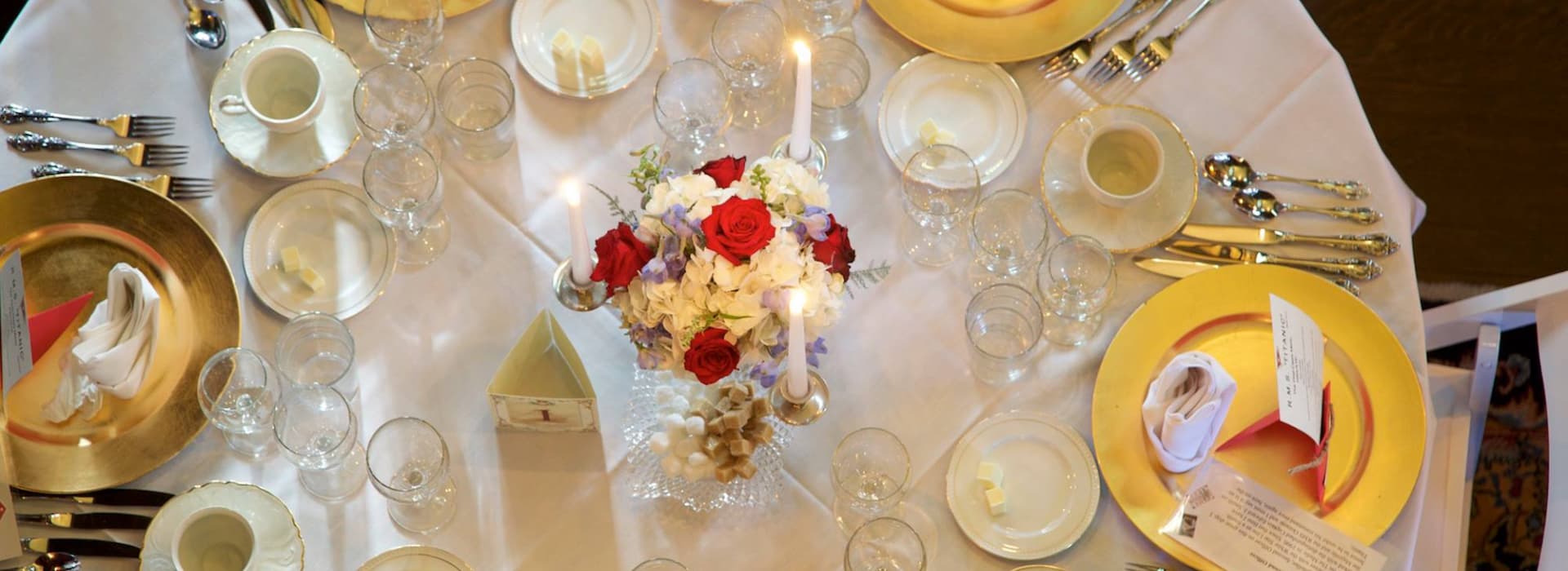 A beautifully set dining table with gold-rimmed plates, sparkling glasses, candles, and a floral centerpiece.