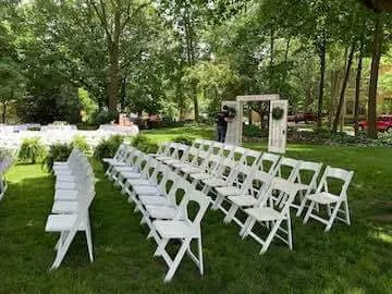 A sunny outdoor setting with white folding chairs arranged for an event, featuring an archway in the background.