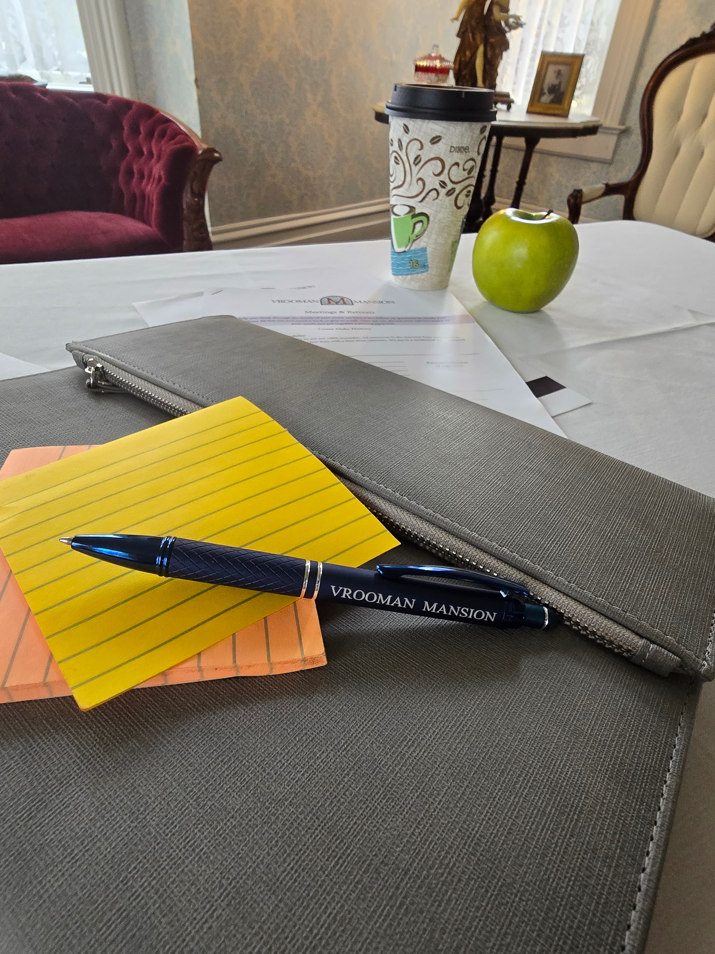 A pen, sticky notes, an apple, a coffee cup, and documents are arranged on a table with a faintly patterned background.