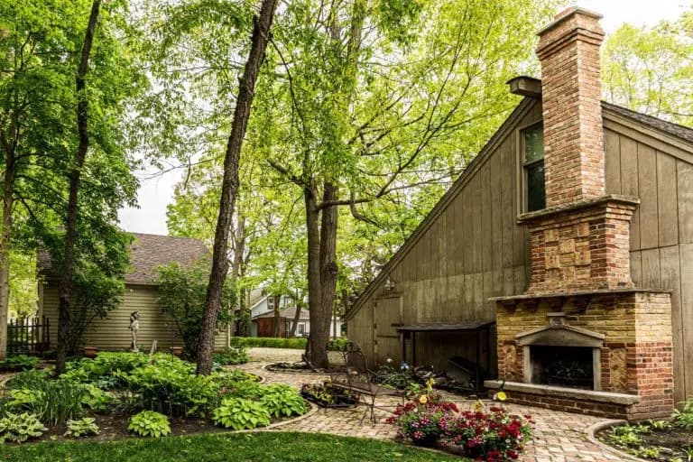 A landscaped outdoor area featuring a brick chimney and lush green trees.
