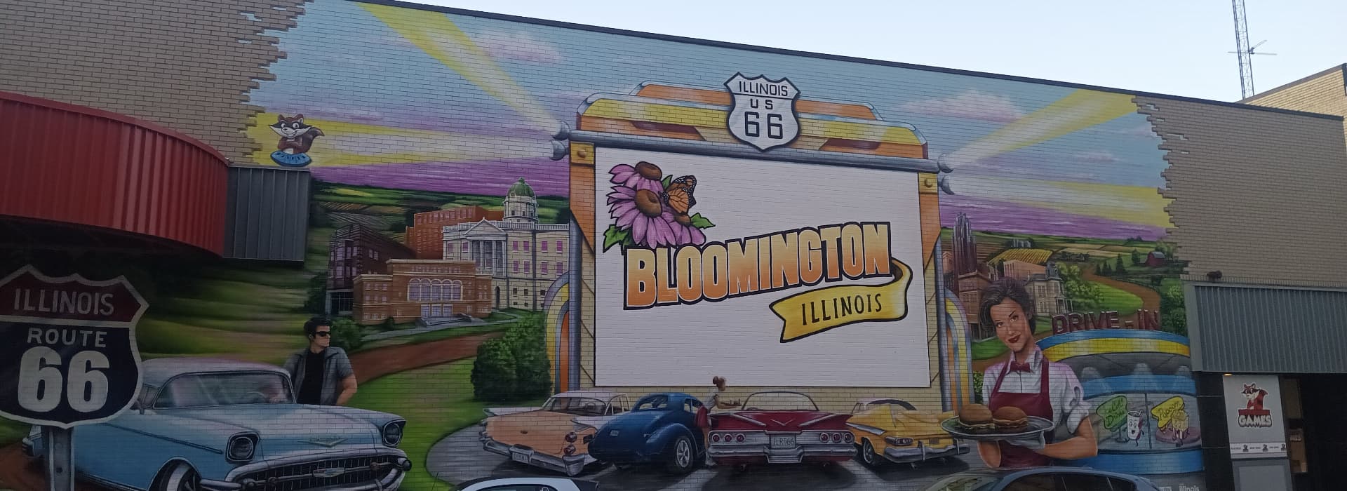 A colorful mural featuring the text "Bloomington, Illinois" along with vintage cars and a drive-in motif.