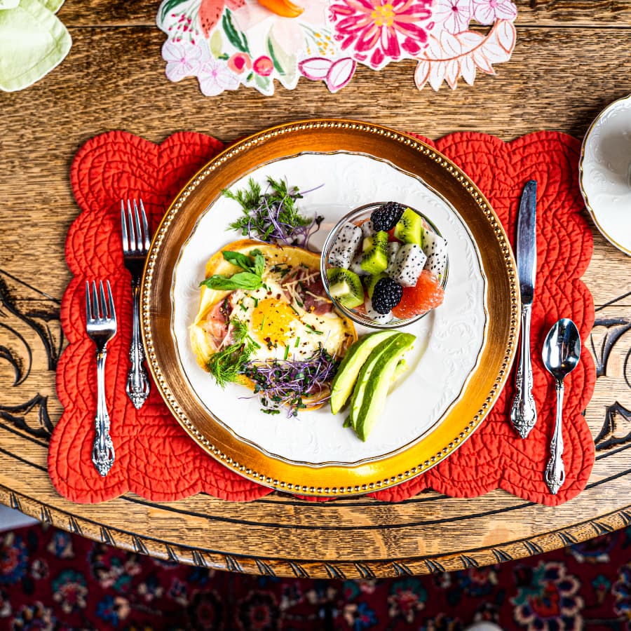 A beautifully arranged plate featuring an omelette, fruit salad, and fresh herbs on a colorful table setting.