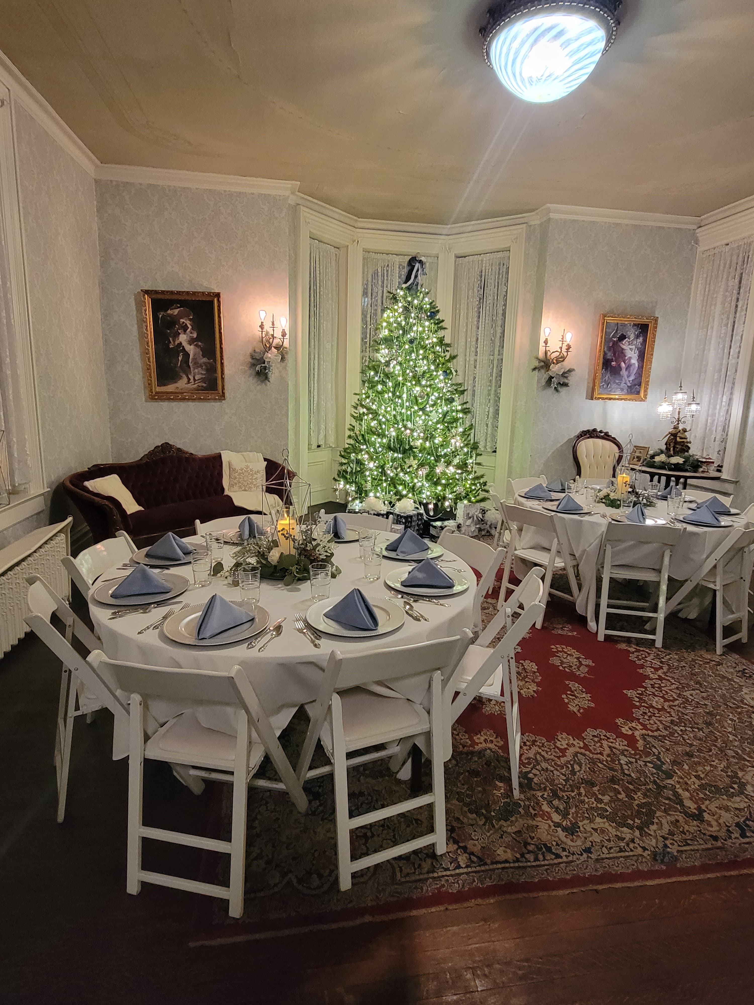 A festive dining room decorated for a holiday gathering, featuring a lit Christmas tree and elegantly set tables.