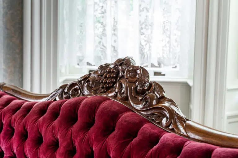 A close-up of an ornate wooden chair back with red tufted upholstery.