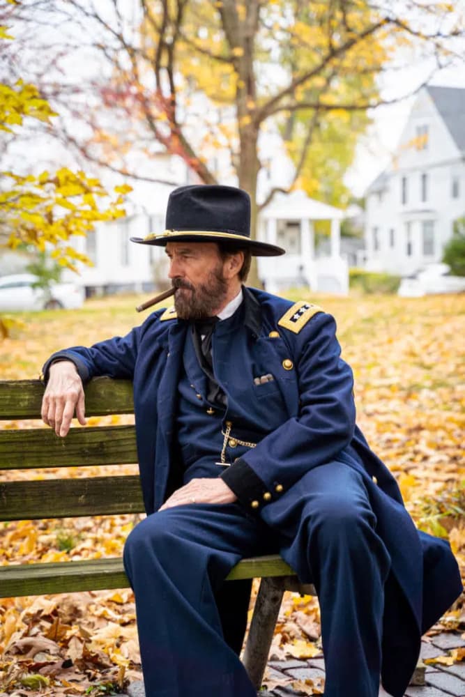 A man dressed in a historical military uniform sits on a bench amid fallen autumn leaves.