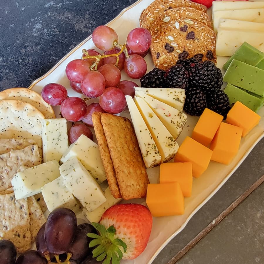 A colorful platter featuring various cheeses, crackers, fruits, and cookies.