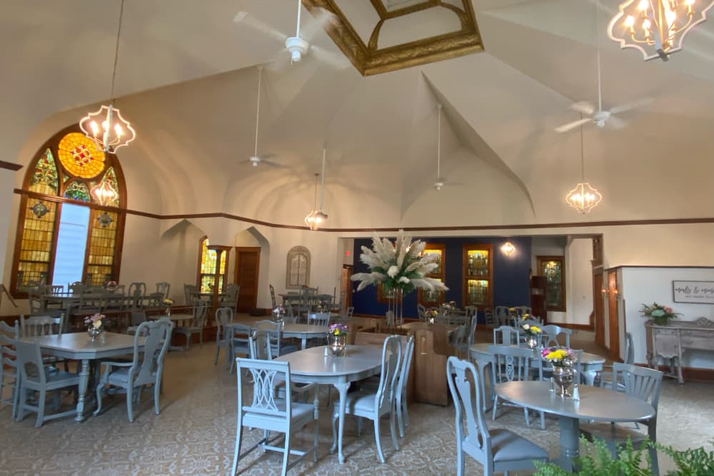 A spacious dining area featuring elegant gray tables and chairs, stained glass windows, and decorative lighting.
