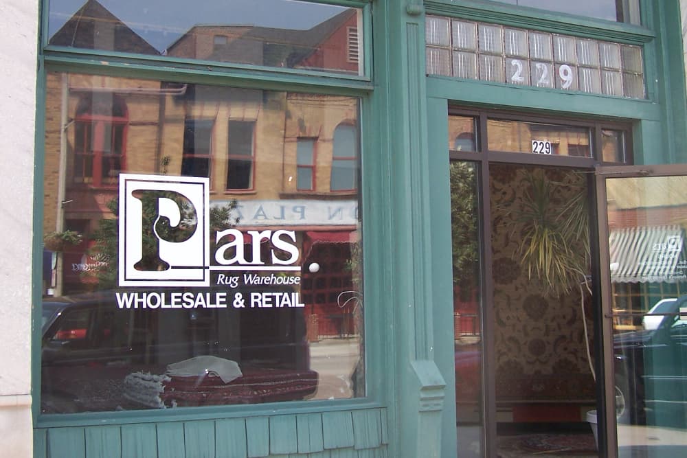 A storefront window displaying the sign for "Pars Rug Warehouse" with the address 229.