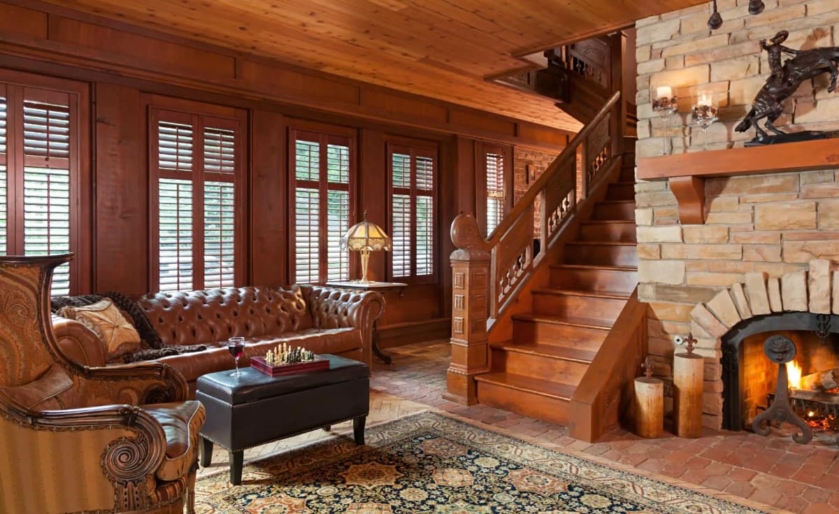 Cozy wooden living room featuring a leather sofa, a stone fireplace, and a staircase.