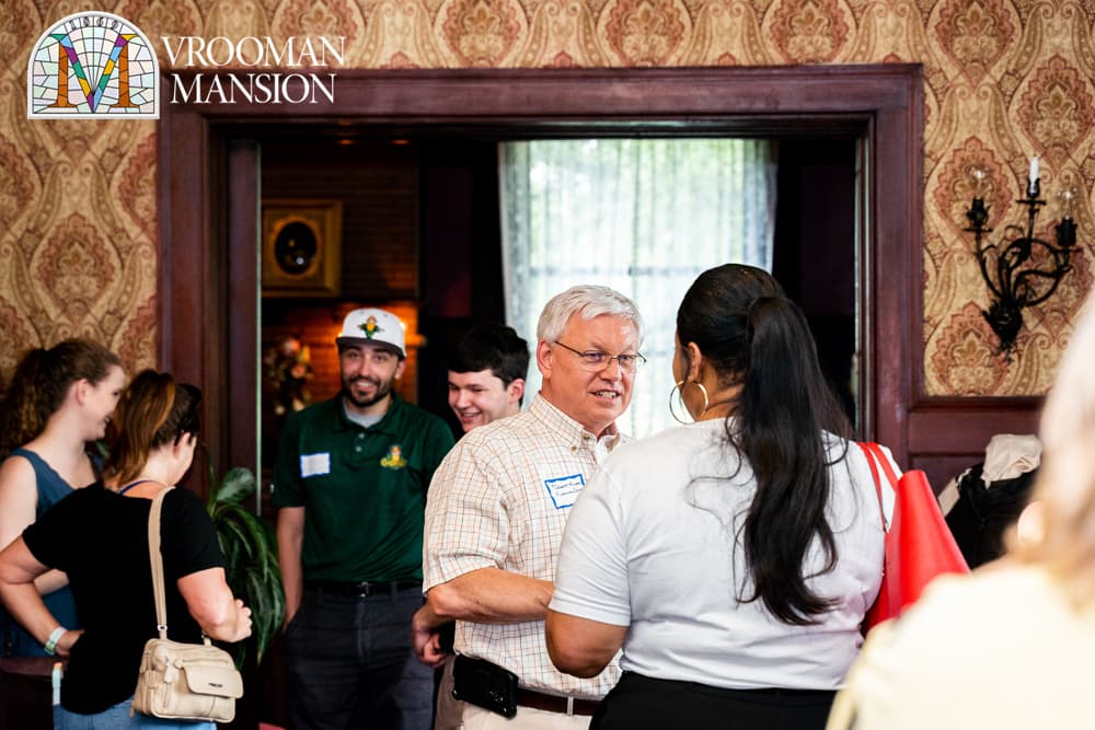 A group of people socializes in a warmly decorated room at Vroonman Mansion.