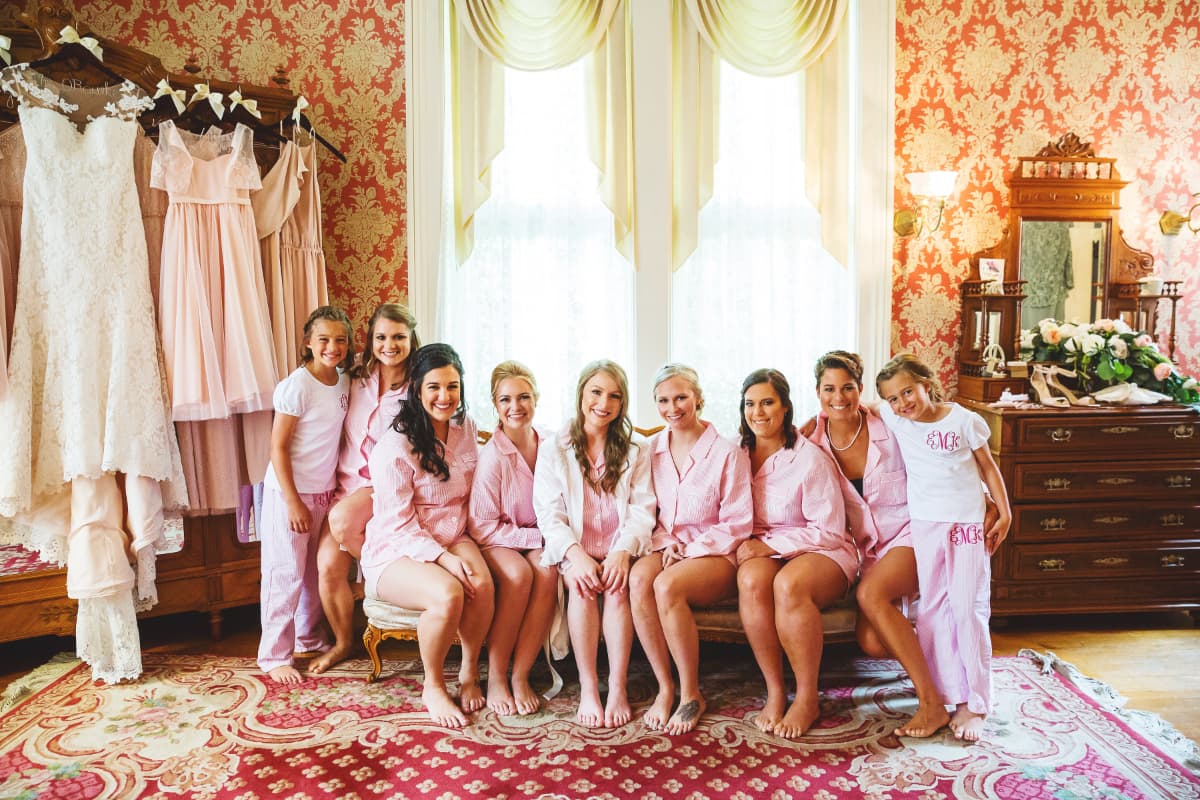 A group of bridesmaids in coordinating pajamas poses together in a beautifully decorated room.