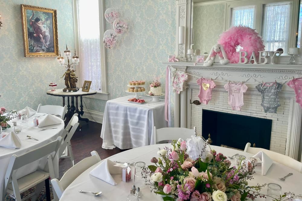 A elegantly decorated room for a baby shower featuring a floral centerpiece, a dessert table, and pink-themed decorations.