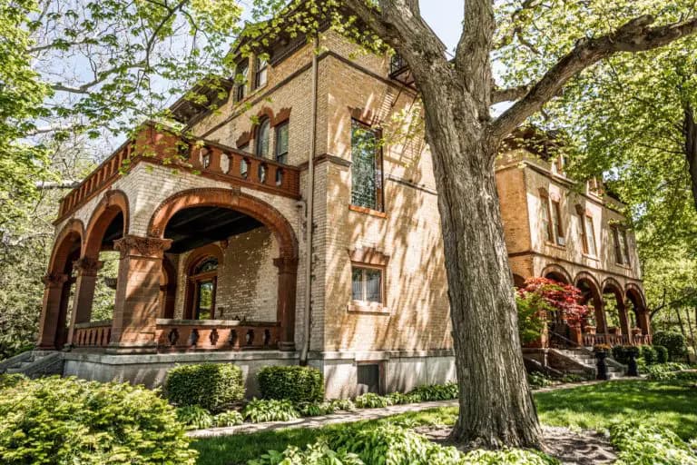 A historic two-story brick mansion surrounded by lush greenery and large trees.
