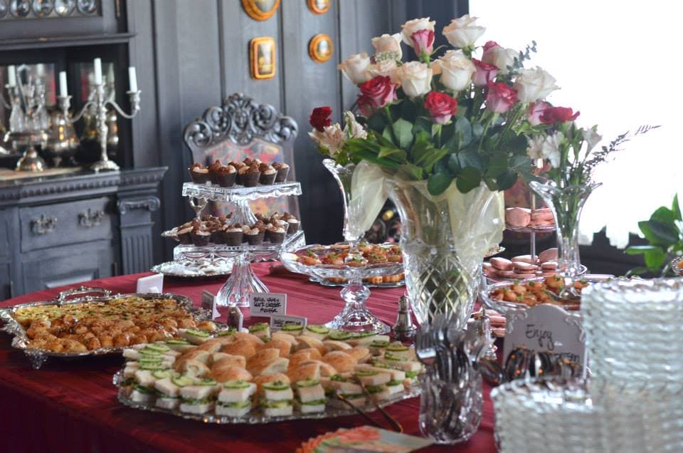 A beautifully arranged table featuring an assortment of pastries, sandwiches, and vibrant flowers in a lavish setting.