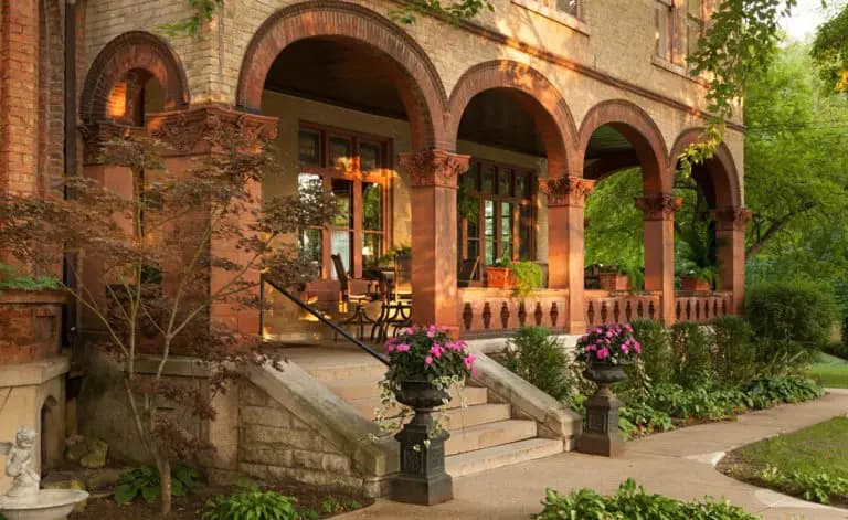 A welcoming porch with arched columns, potted flowers, and lush greenery.
