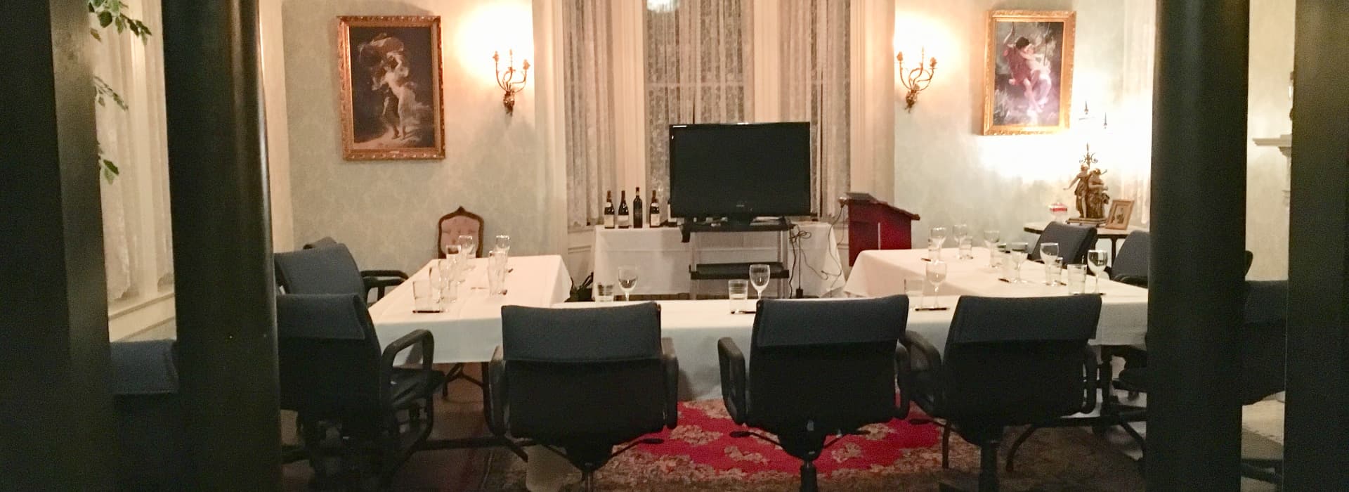 A formal dining room set for a meeting, featuring a long table, chairs, and a television.