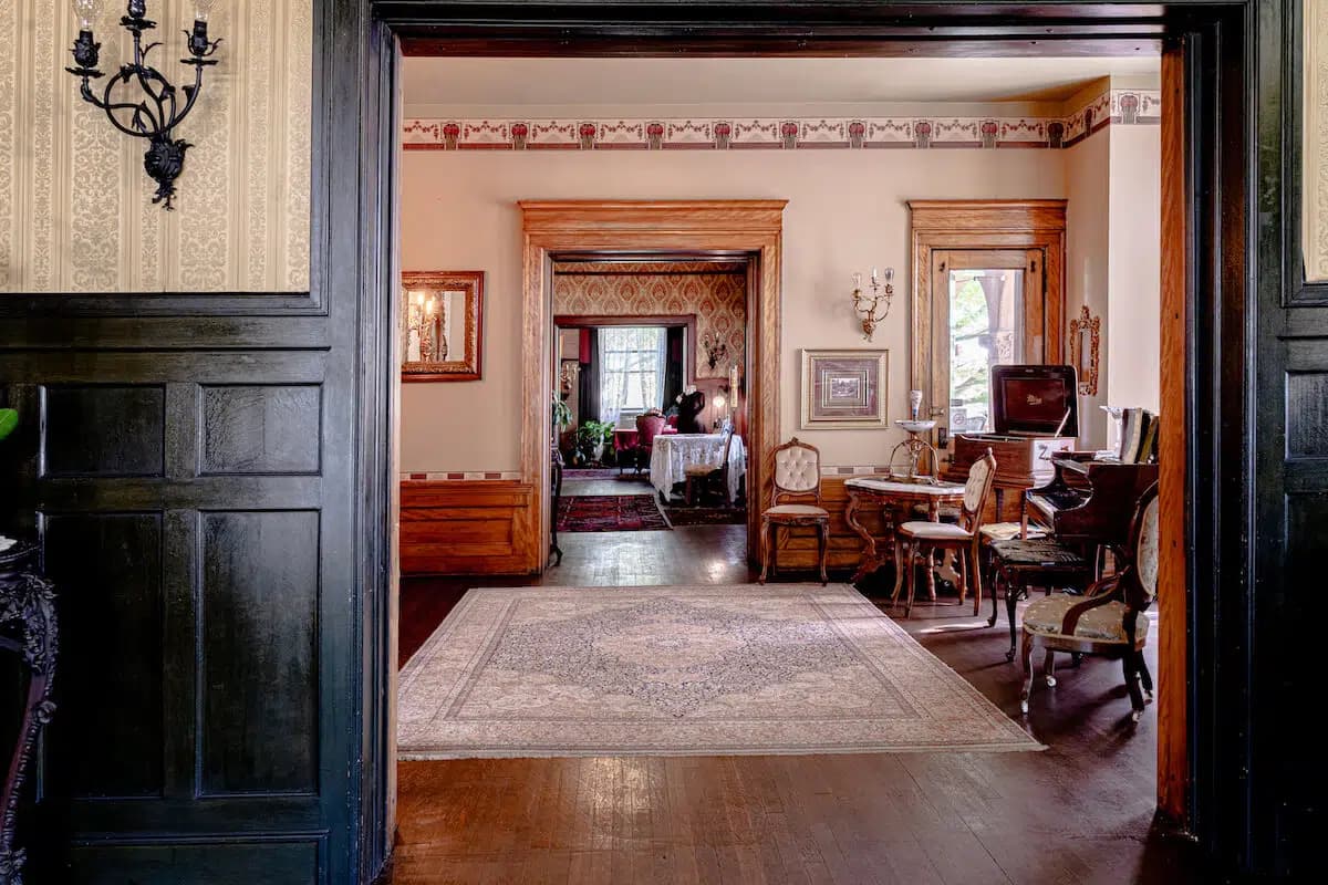A view through a doorway into an elegantly decorated living room featuring vintage furniture and detailed wallpaper.