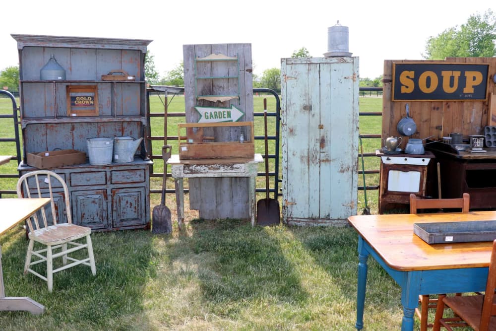 A collection of vintage furniture and decor items displayed outdoors, including shelves, chairs, and kitchenware.