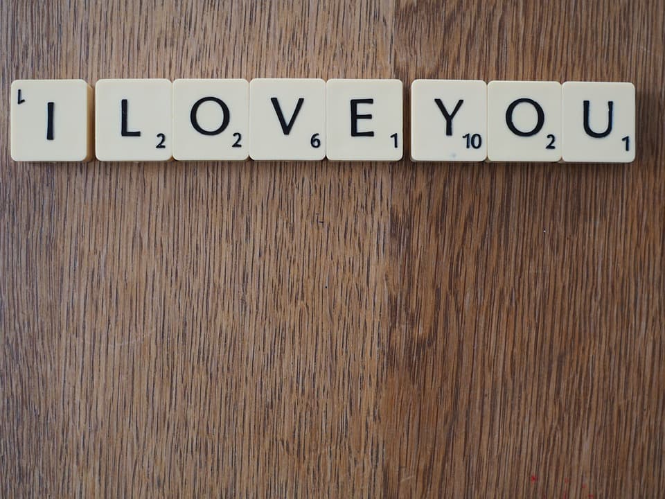 Scrabble tiles spell out "I LOVE YOU" on a wooden surface.