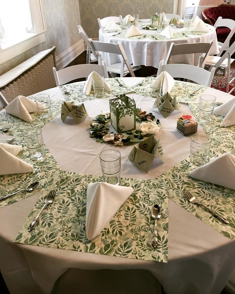 A beautifully arranged dining table with green leaf-patterned tablecloths, elegant napkin folds, and decorative centerpieces.