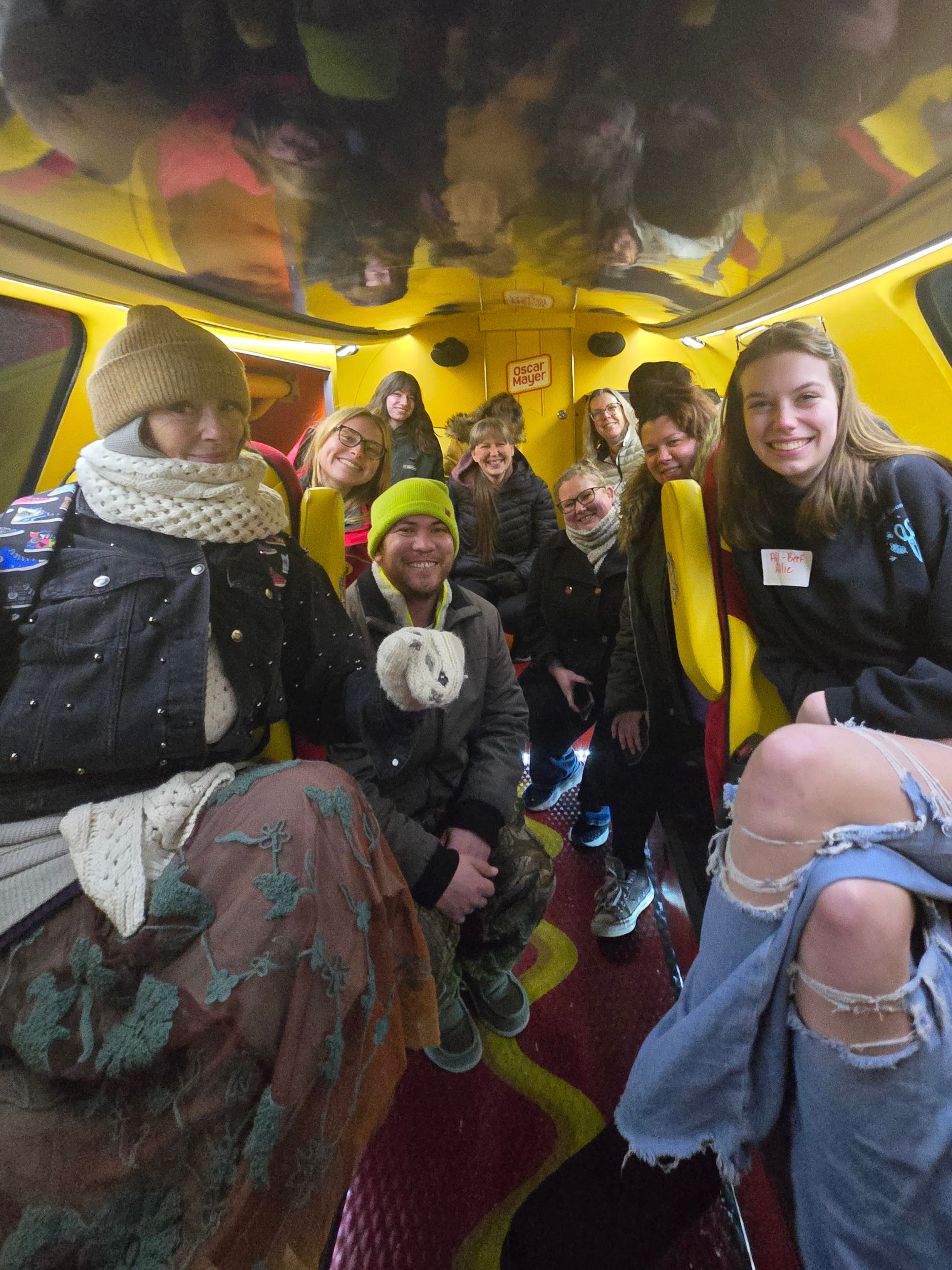 A group of ten people are sitting inside a colorful vehicle with a yellow interior, smiling at the camera.