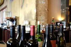 Close-up shot of several wine bottles of various colors and shapes arranged on a table, with a blurred background of a restaurant or bar. Close-up shot of several wine bottles of various colors and shapes arranged on a table, with a blurred background of a restaurant or bar.