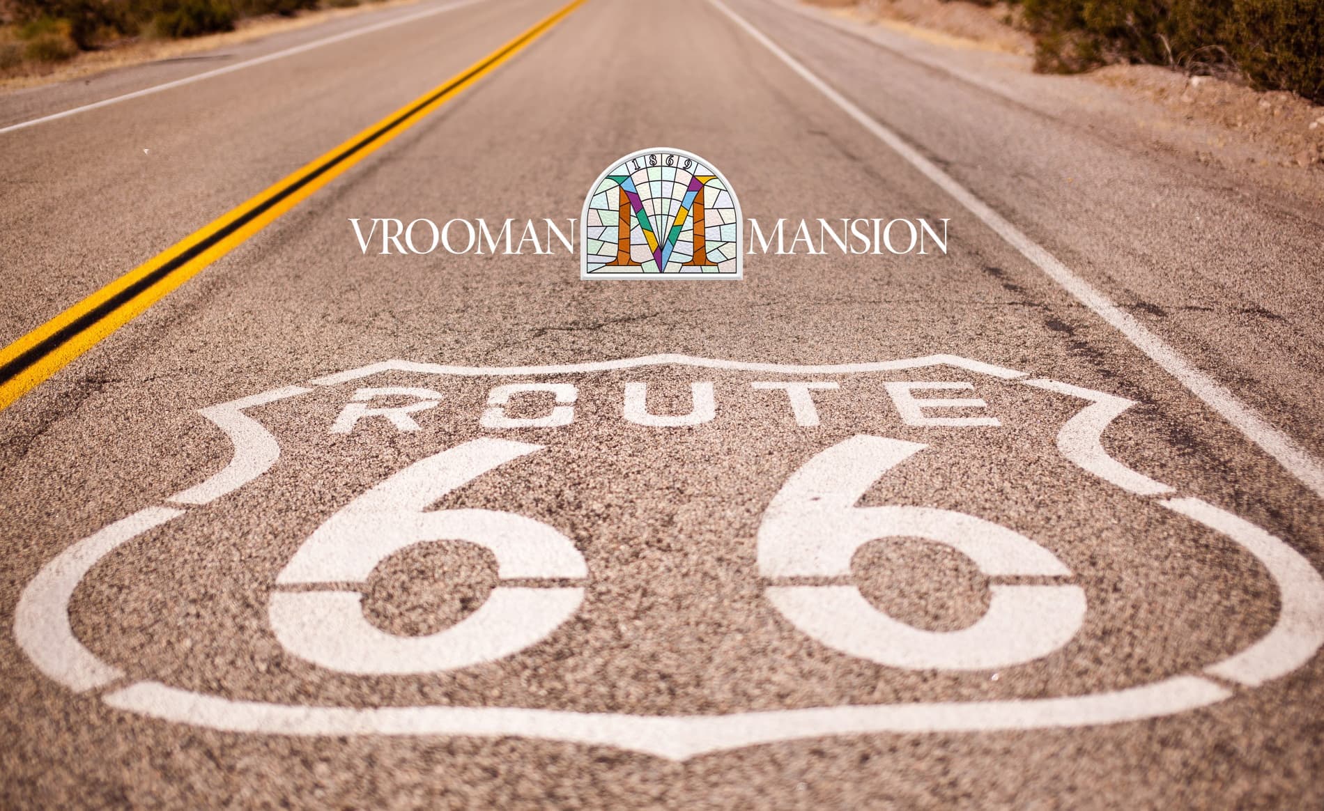 Close-up of a Route 66 road marking with the Vrooman Mansion logo placed above it, showing the road stretching into the distance. Close-up of a Route 66 road marking with the Vrooman Mansion logo placed above it, showing the road stretching into the distance.