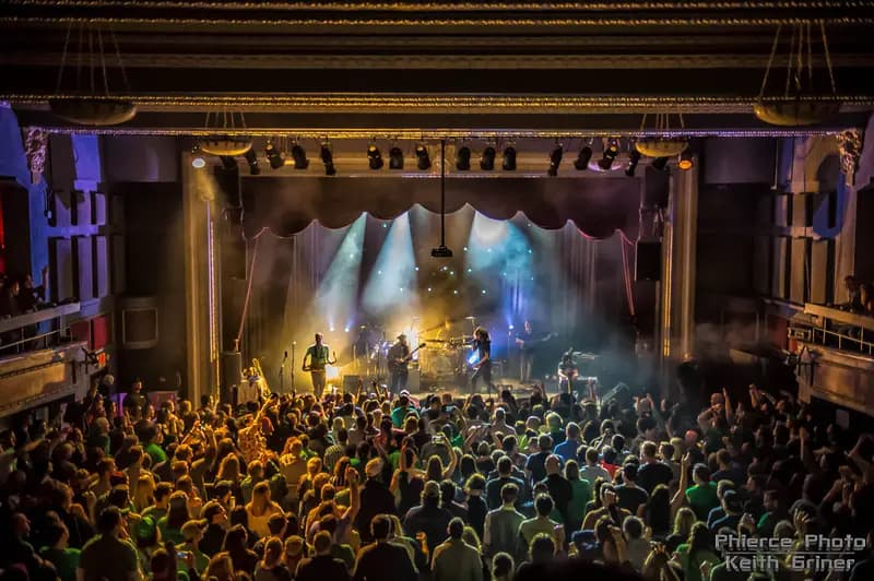 A group of people watching a concert on a stage with musicians performing and colorful lights behind them. A group of people watching a concert on a stage with musicians performing and colorful lights behind them.