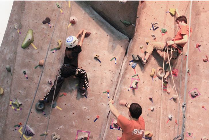 Two young men and a boy climbing a tall indoor rock wall