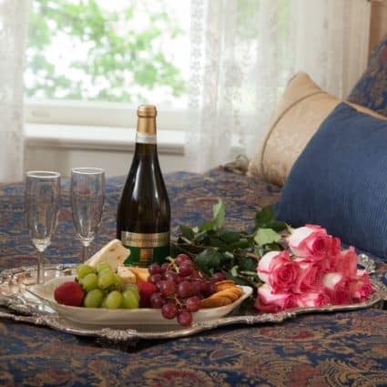 fruit, cheese, crackers, roses and champagne on the bed in Julia Vrooman's Suite