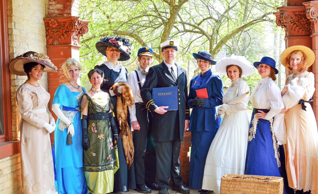 Group of people standing on the covered porch wearing old-fashioned elegant clothing in blues, whites and other colors