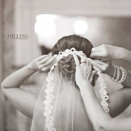 Black and white photo of a woman's hands helping a bride adjust her veil