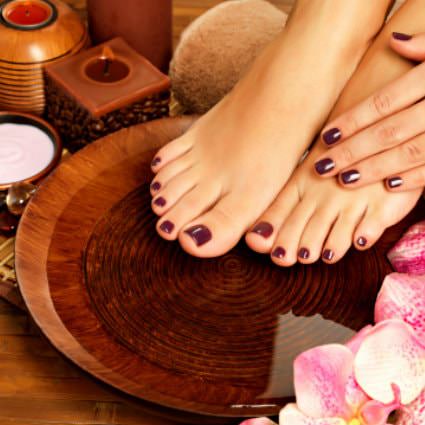 Woman's feet and left hand freshly manicured with dark red polish